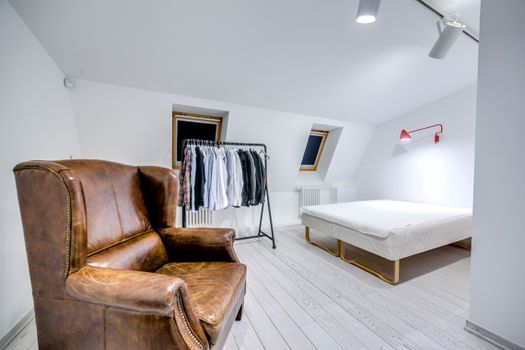 Stylish minimalist bedroom featuring a brown leather armchair, clothing rack, and simple design.