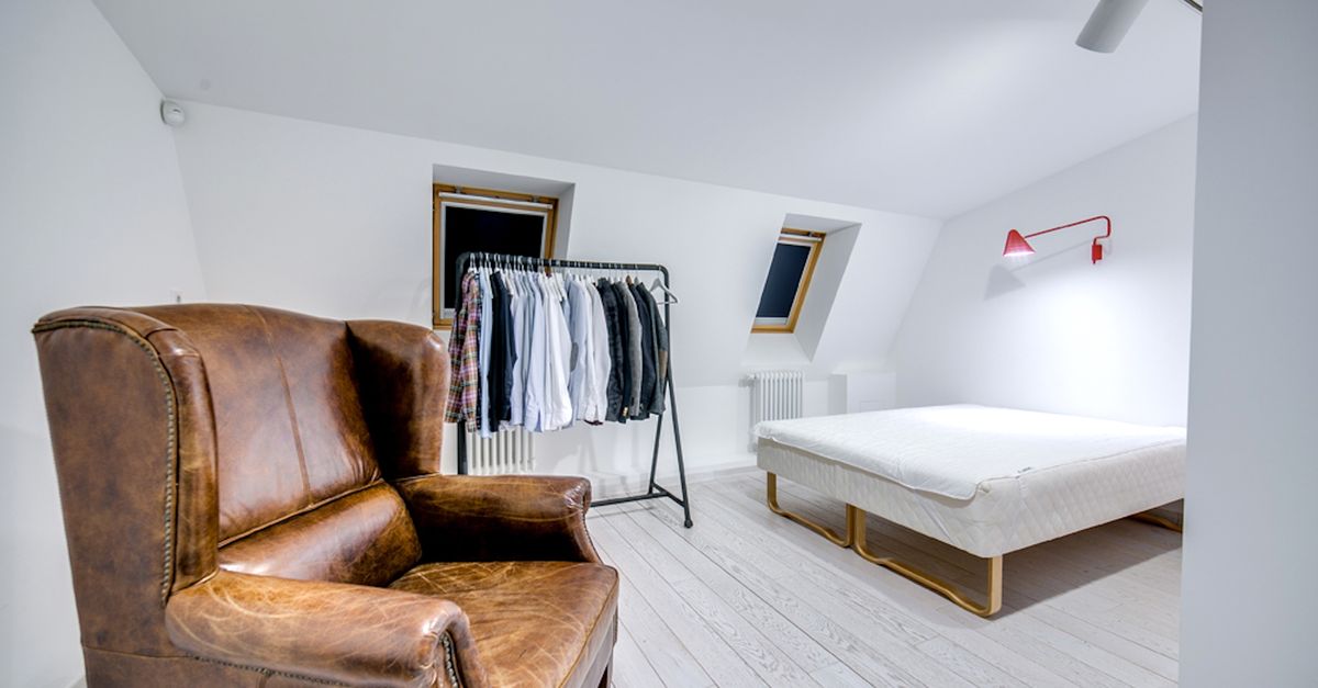 Stylish minimalist bedroom featuring a brown leather armchair, clothing rack, and simple design.