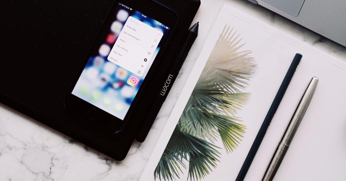 A close-up view of a modern workspace featuring a smartphone, Wacom drawing tablet, and writing tools on a marble surface.