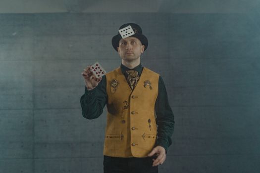 A magician in a brown vest performing a card trick indoors, showcasing skill and magic.