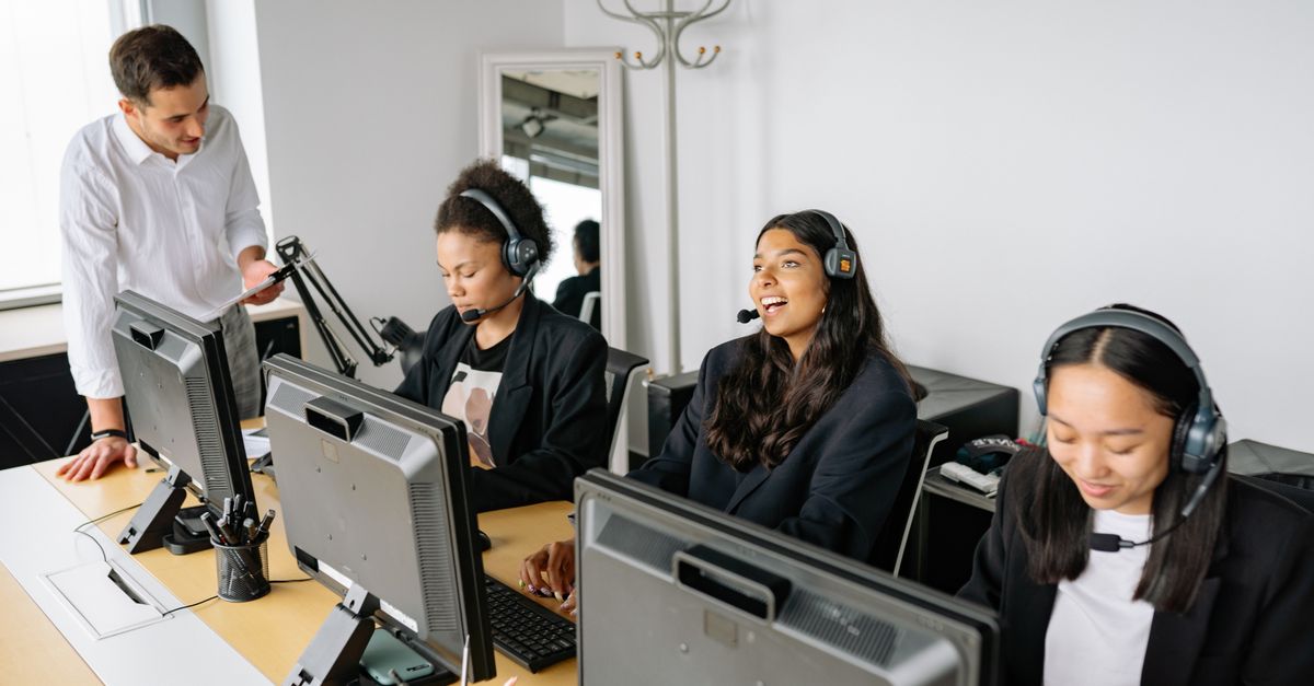 A diverse team of customer service representatives working in an office setting, wearing headsets and using computers.