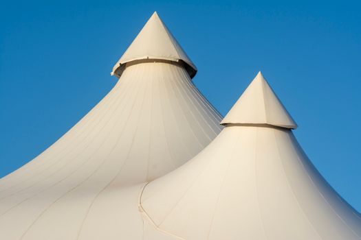 Two elegant white tent tops with sharp peaks set against a bright blue sky, showcasing modern architecture.