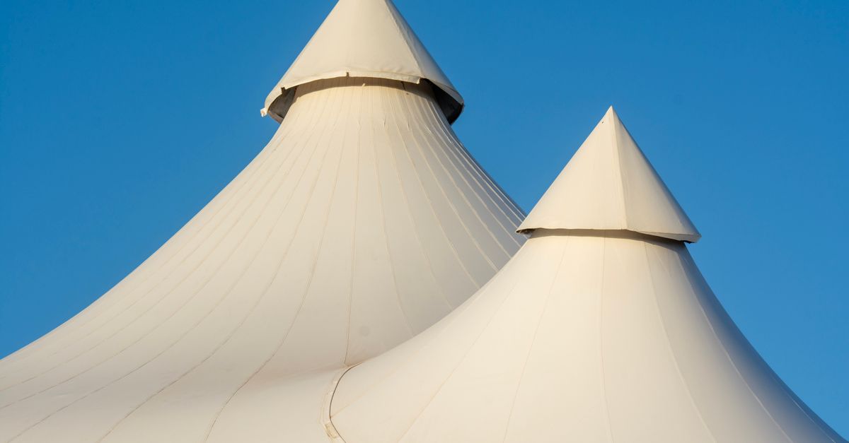 Two elegant white tent tops with sharp peaks set against a bright blue sky, showcasing modern architecture.