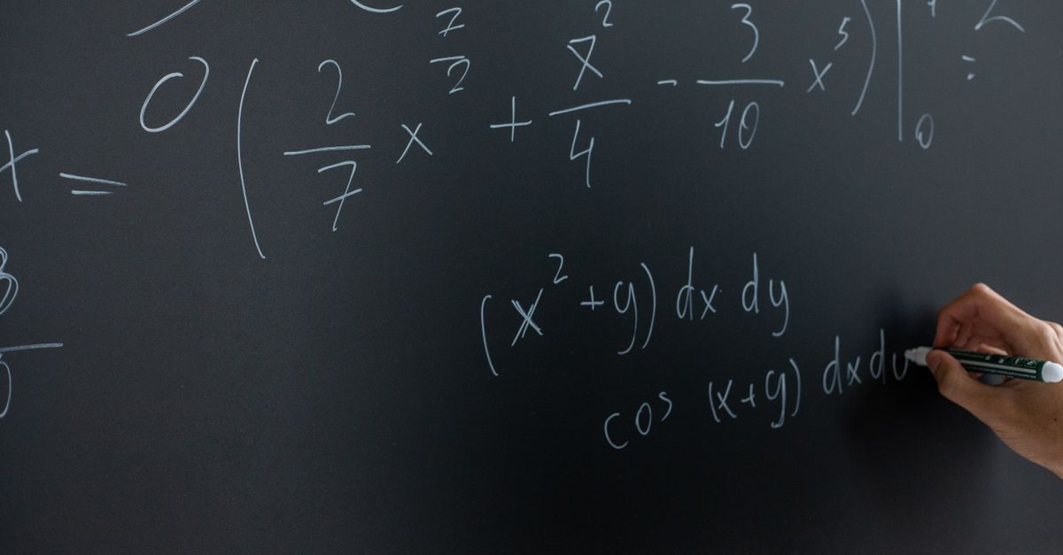 Hand writing mathematical equations on a chalkboard in a classroom setting.