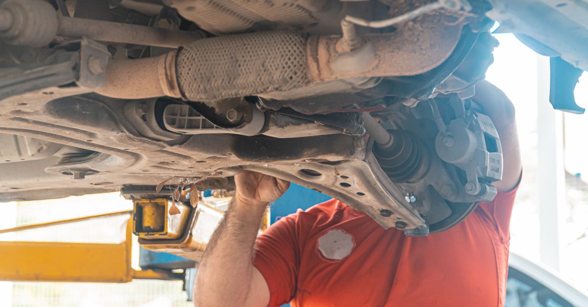 Mechanic working under a vehicle, inspecting the undercarriage in a repair garage, ensuring safety and performance.