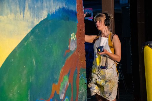 Female artist painting a vibrant mural while listening to music in an indoor studio environment.