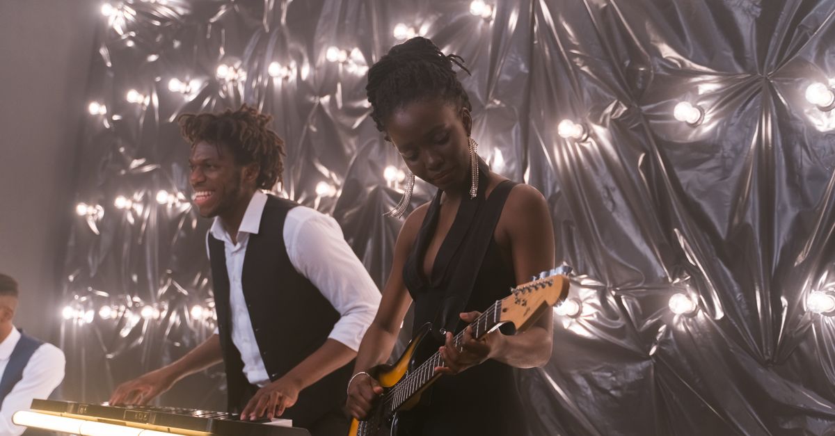 Energetic live performance by a band featuring electric guitar and keyboard players under creative lighting.