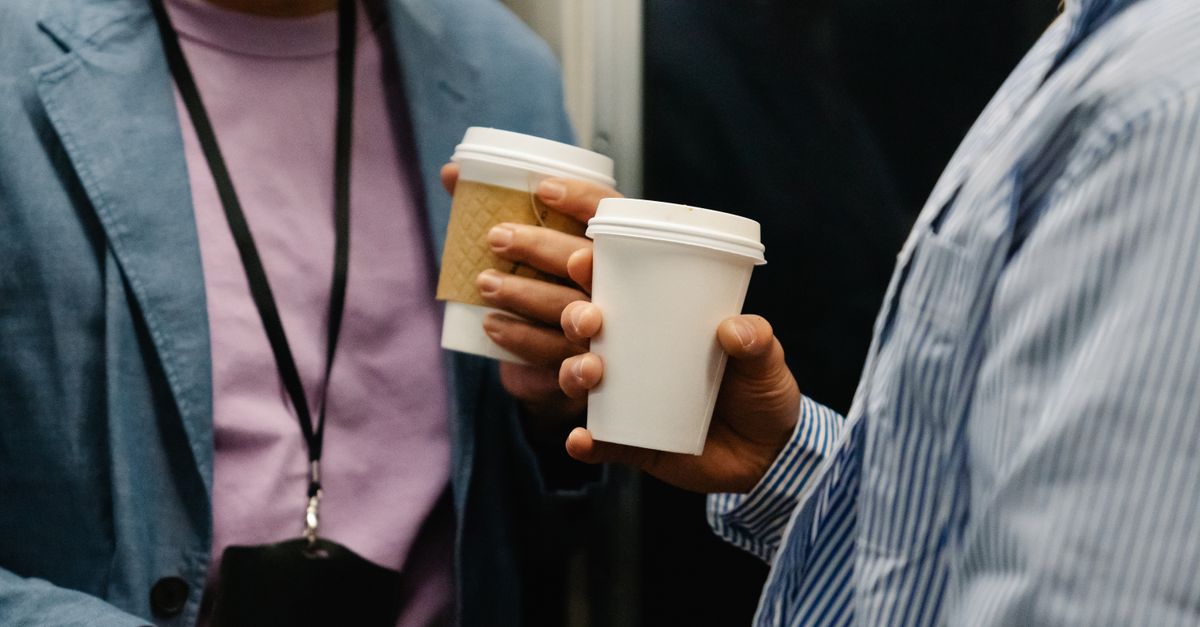 Two professionals holding coffee cups during a casual meeting indoors.