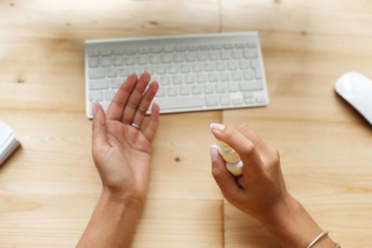 Close-up of hands using sanitizer spray near a keyboard on a wooden desk.