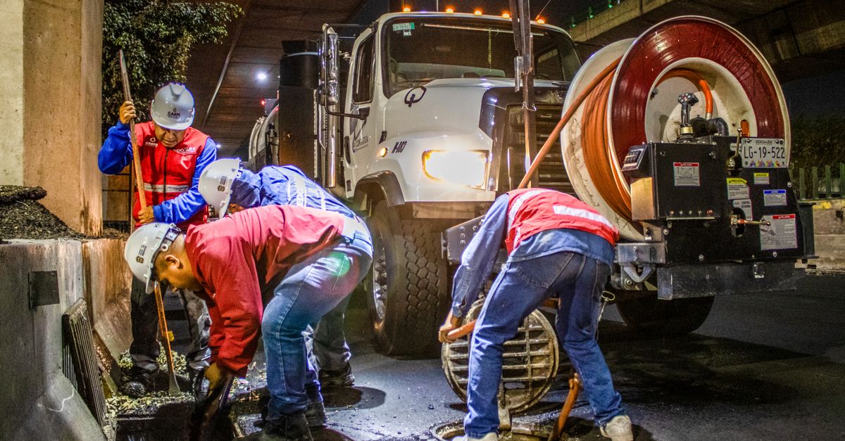 Street workers cleaning drainage at night with machinery under a bridge.