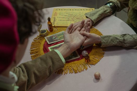 Close-up of a fortune-teller performing a palm reading with tarot cards on a decorated table.