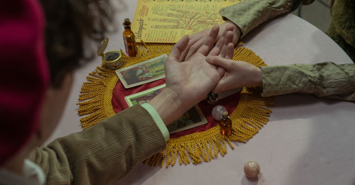 Close-up of a fortune-teller performing a palm reading with tarot cards on a decorated table.