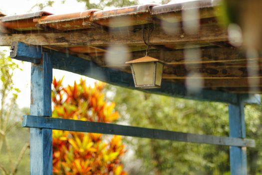 Rustic wooden structure with a hanging lamp under a rainy sky, providing a cozy outdoor setting.