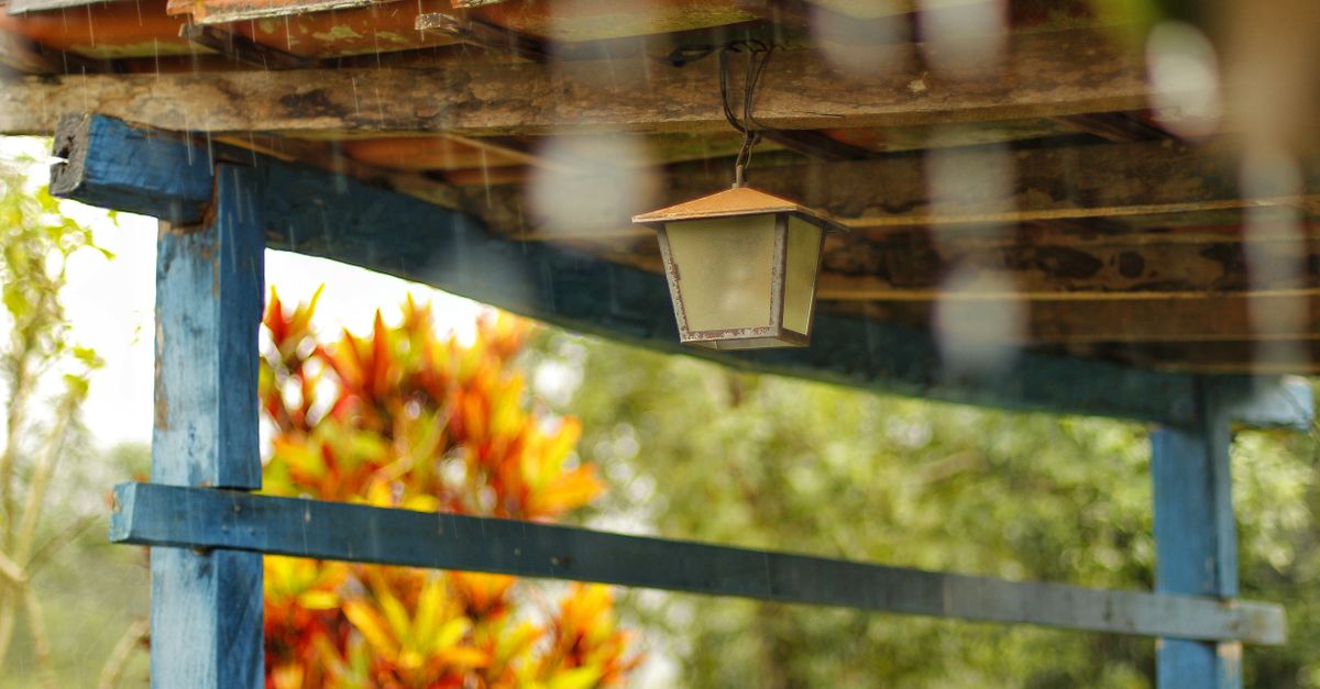 Rustic wooden structure with a hanging lamp under a rainy sky, providing a cozy outdoor setting.
