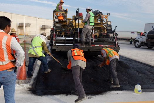 Construction workers laying asphalt on a road with heavy machinery.
