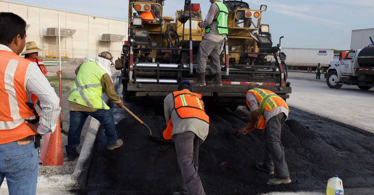 Construction workers laying asphalt on a road with heavy machinery.