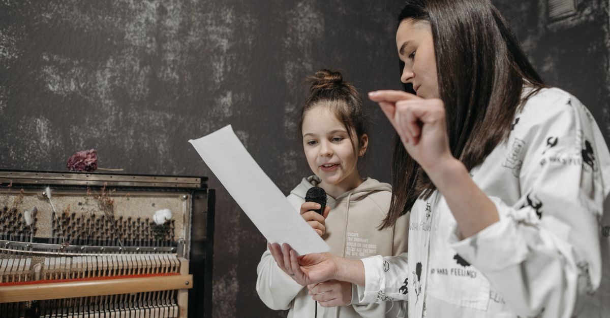 A girl receiving a singing lesson with a microphone in a music studio.