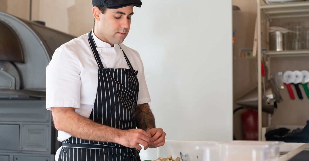A chef in traditional attire prepares food in a kitchen setting, showcasing culinary skills.