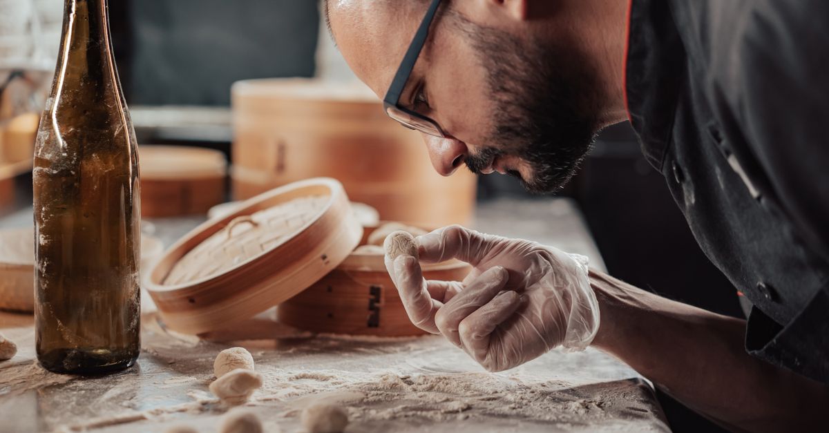 A chef inspects a dough ball on a flour-dusted counter, emphasizing precise food preparation.