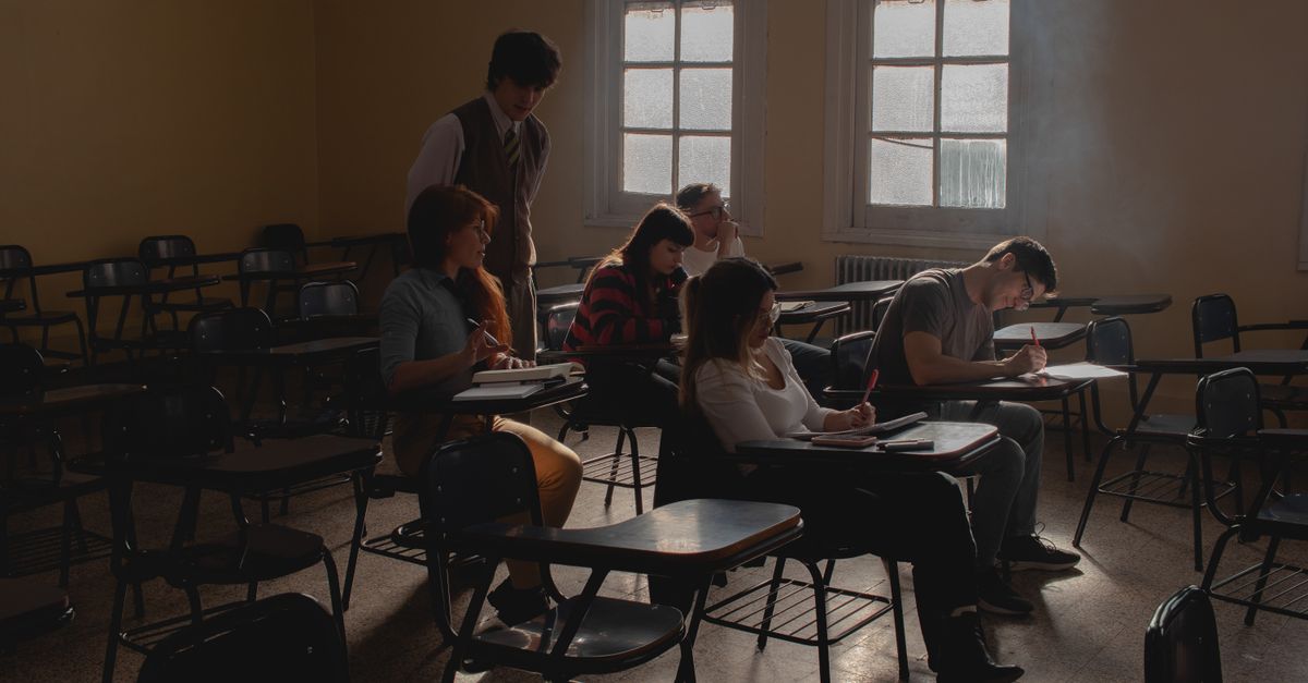 Group of students studying in a dimly lit classroom with vintage desks and natural light.
