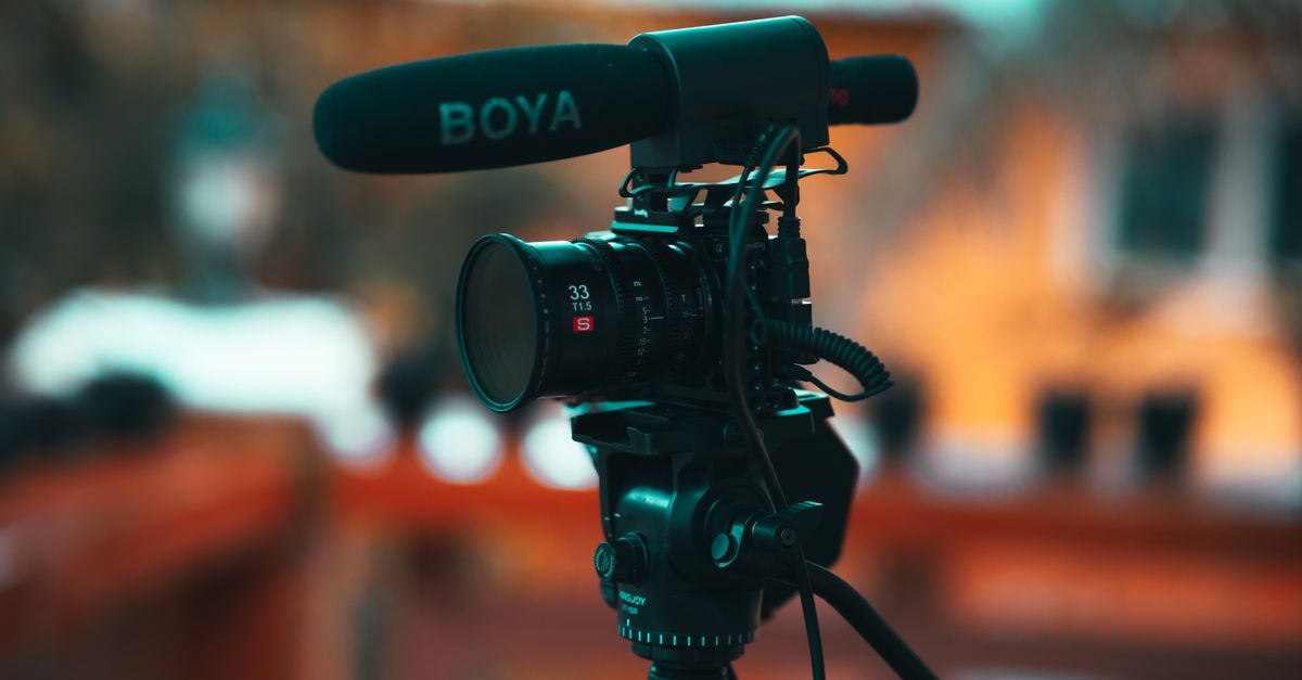 Close-up of a professional video camera mounted on a tripod with a microphone outdoors.