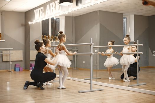 Ballet instructor helps young girls in tutus practice at a mirrored barre.