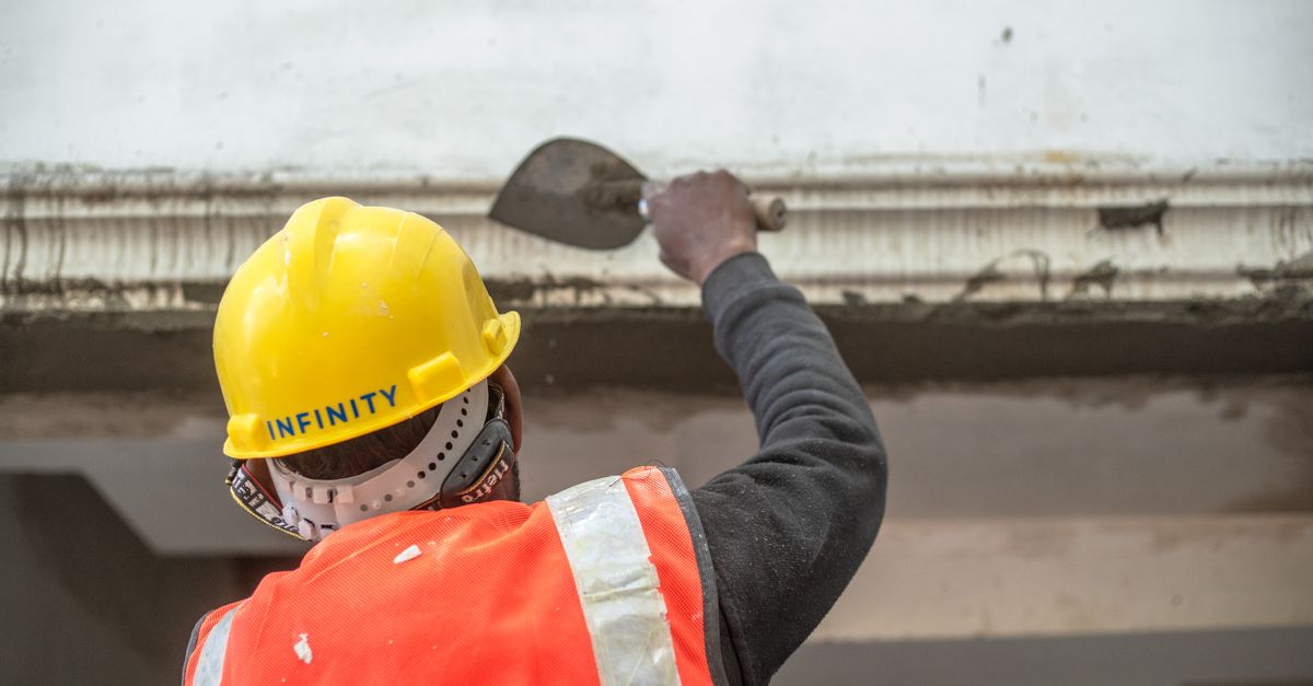 A construction worker in safety gear renovating an interior wall in Delhi, India.