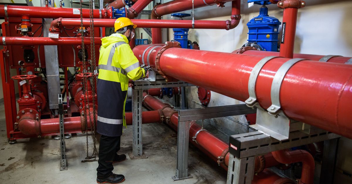 Engineer with safety gear inspecting red industrial piping system indoors.