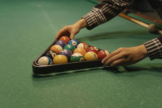 Adult arranging billiard balls into a triangle rack on a pool table. Perfect setup for a game of billiards.