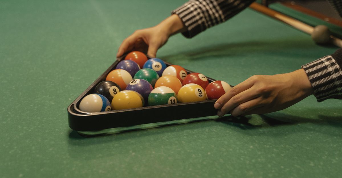 Adult arranging billiard balls into a triangle rack on a pool table. Perfect setup for a game of billiards.