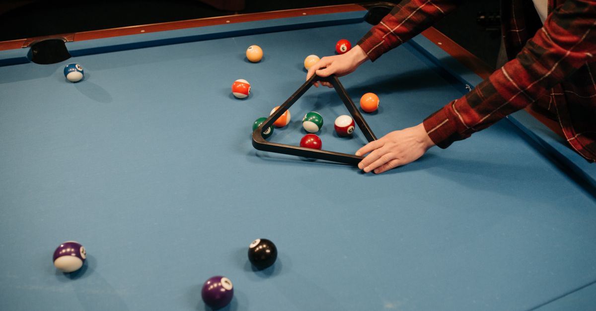 A person arranging billiard balls on a blue pool table in preparation for a game indoors.
