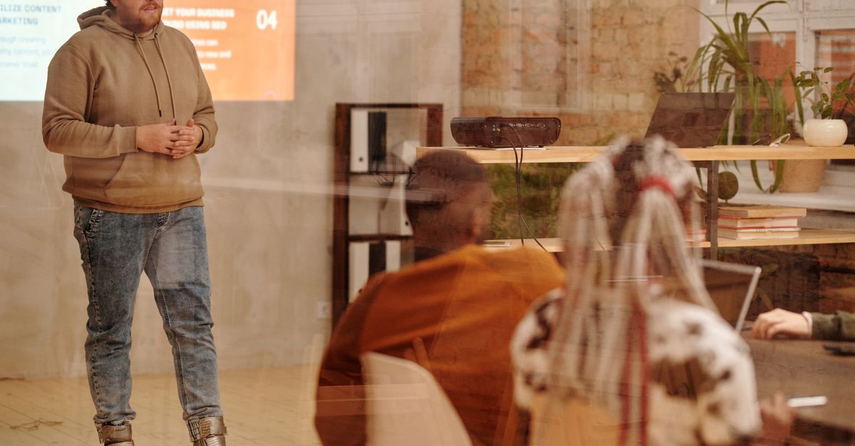 A presenter in casual attire engages an audience in a modern loft setting.