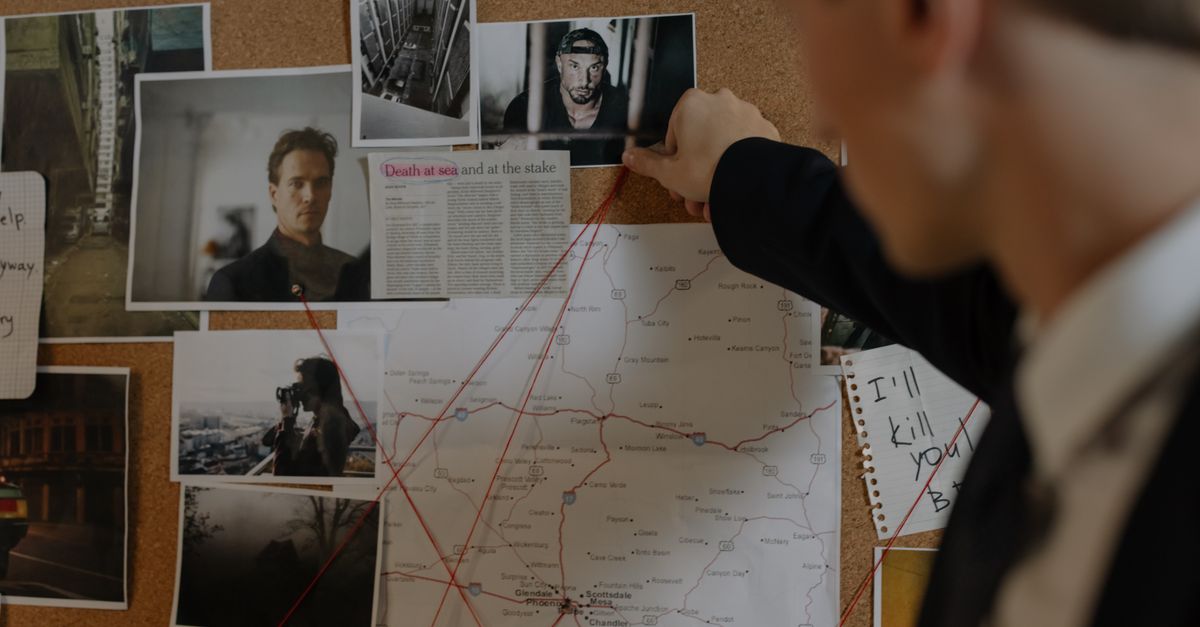 Detective examining a crime investigation board with photos, maps, and notes indoors.