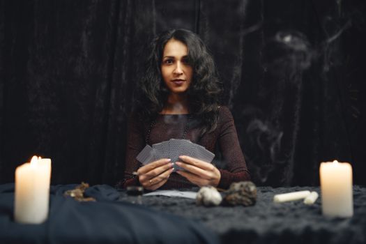 A mysterious woman holds tarot cards in a dimly lit setting, evoking a sense of mysticism and spirituality.