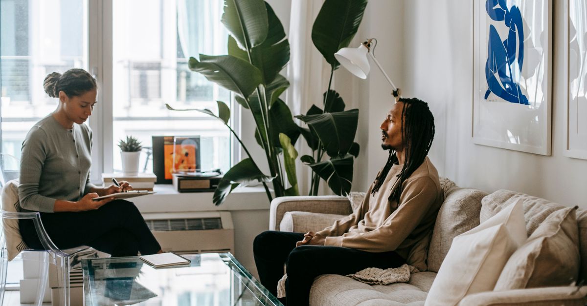 African American female taking notes on paper while speaking with male partner on sofa at home