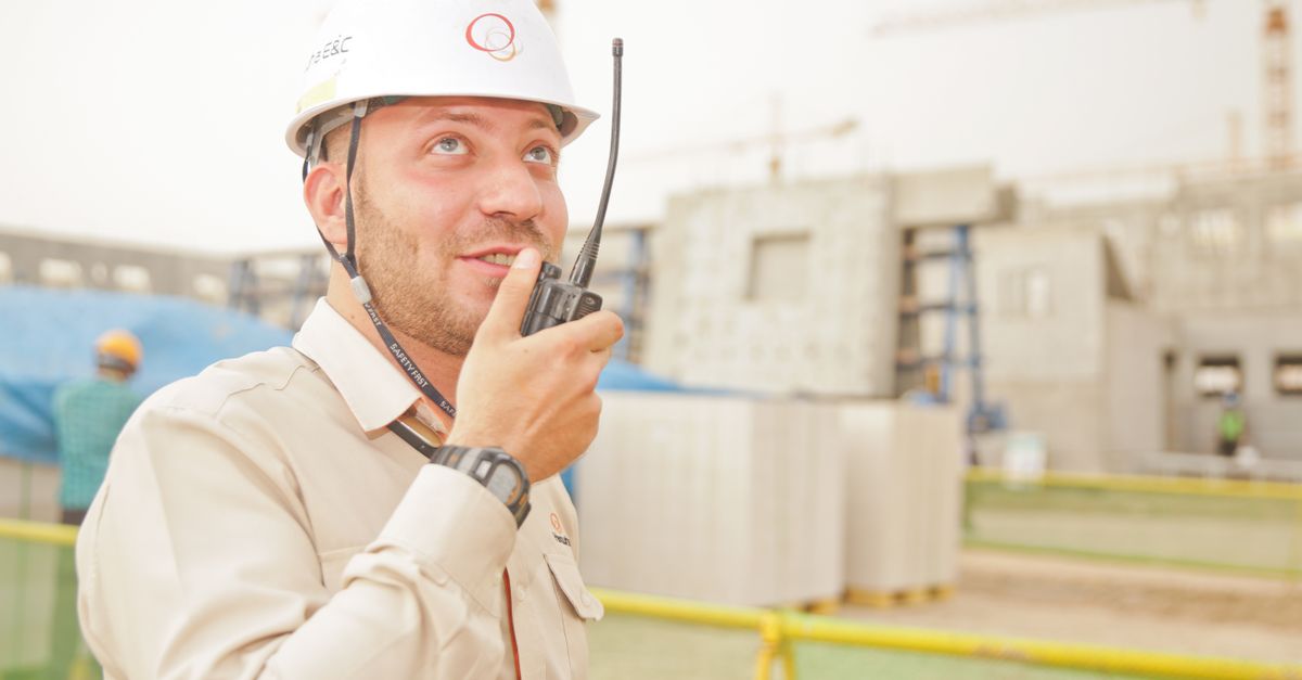 Male construction worker using radio on a building site, wearing a safety helmet, communicating effectively.