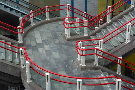 Contemporary staircase with vibrant red railings in a Rotterdam station, showcasing urban architecture.