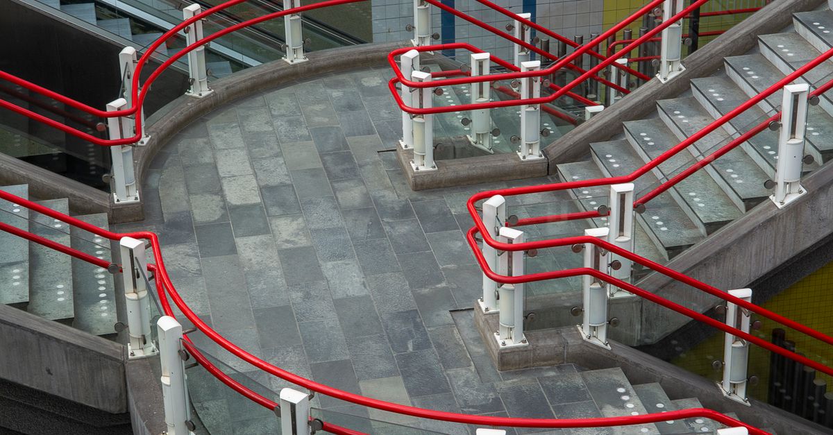 Contemporary staircase with vibrant red railings in a Rotterdam station, showcasing urban architecture.