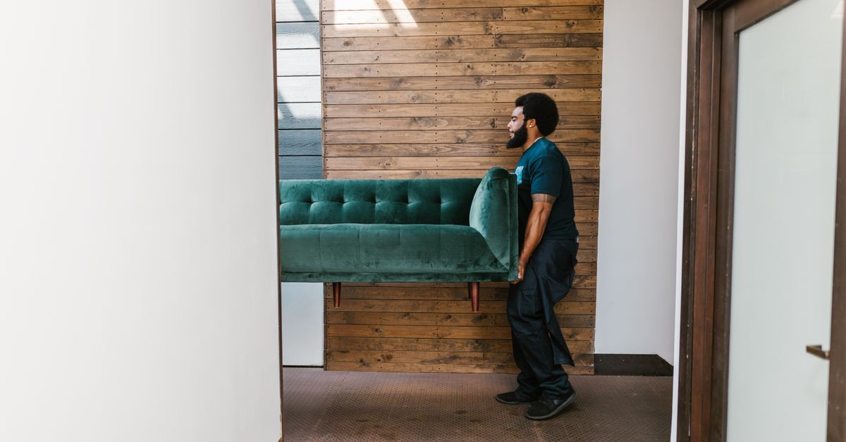 A mover carries a green sofa indoors, showcasing modern interior design and relocation services.