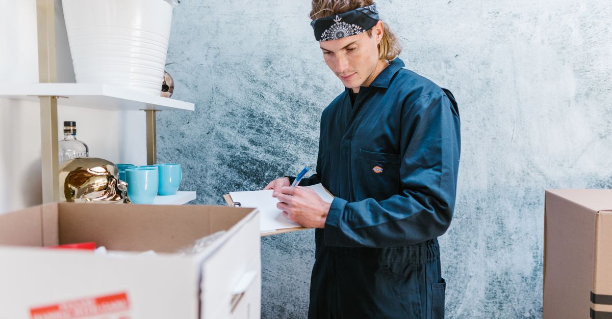 Man wearing overalls and bandana preparing for a home move, surrounded by boxes and fragile items.