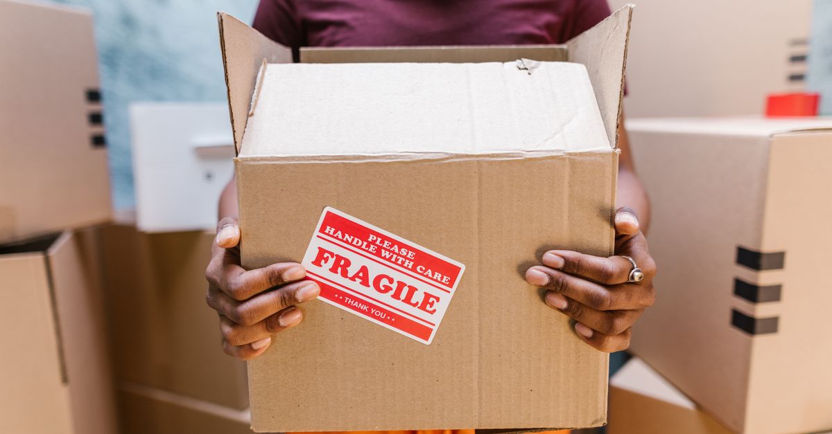 A person holding a cardboard box labeled 'Fragile' during a moving process indoors.