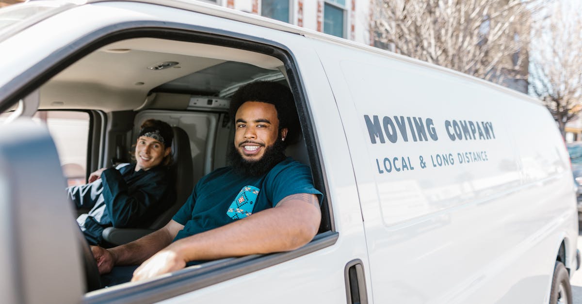 Two movers smiling from their moving company van parked on a sunny day.