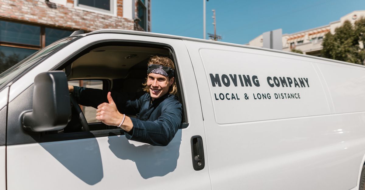 Smiling mover giving thumbs up from a moving company van parked outside.