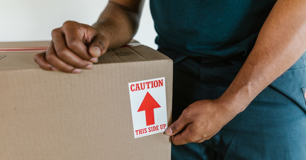 A person handling a moving box with a 'caution this side up' label indoors.