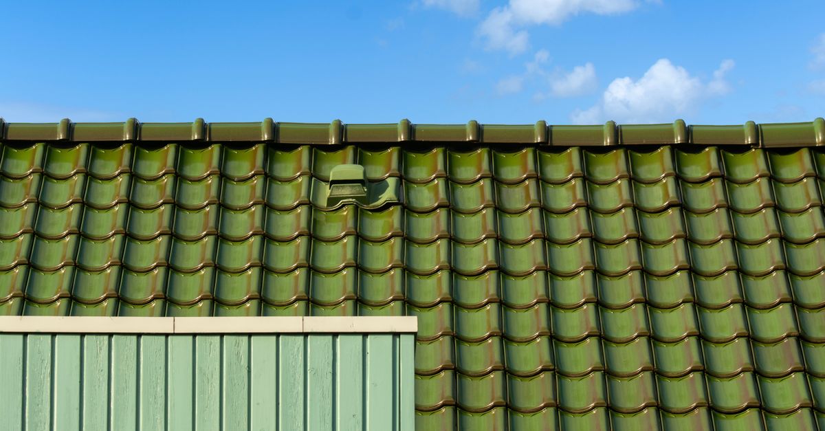 Closeup of a green tiled roof under a bright blue sky, capturing architectural detail and color contrast.