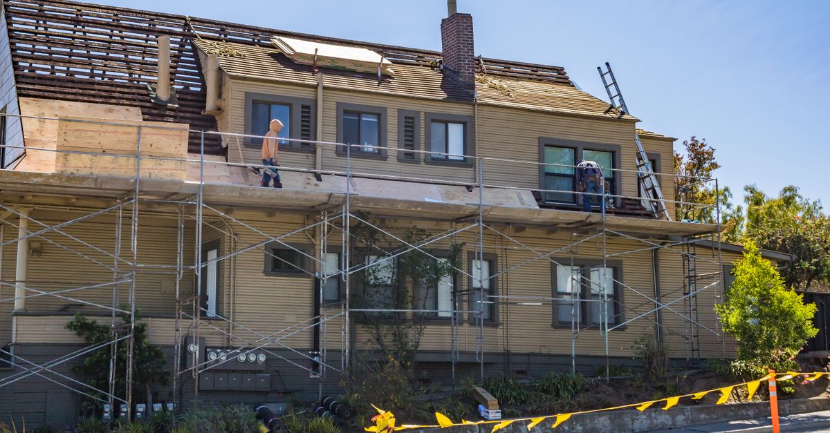 House under renovation with scaffolding and workers fixing the roof on a sunny day.