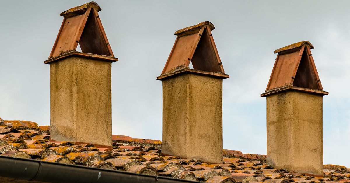 Image of three chimneys with triangular covers on a tiled roof under an overcast sky.