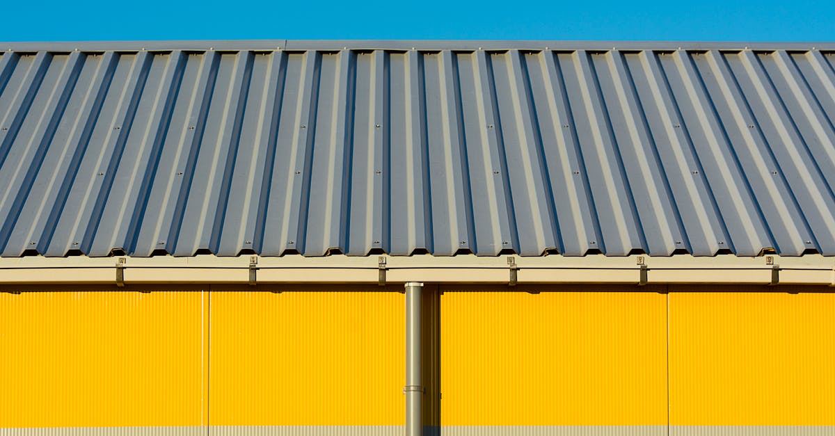 Photo of a yellow warehouse wall with a corrugated metal roof under a clear blue sky.