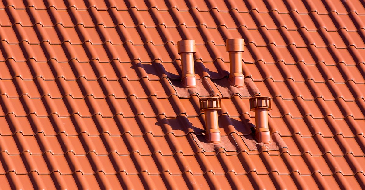 Vibrant red tiled rooftop featuring symmetrical chimneys casting soft shadows in daylight.