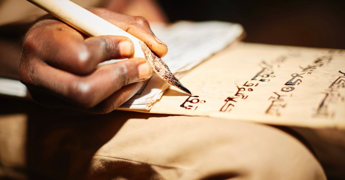Detailed close-up of a person writing on papyrus with a traditional ink pen, highlighting cultural script.